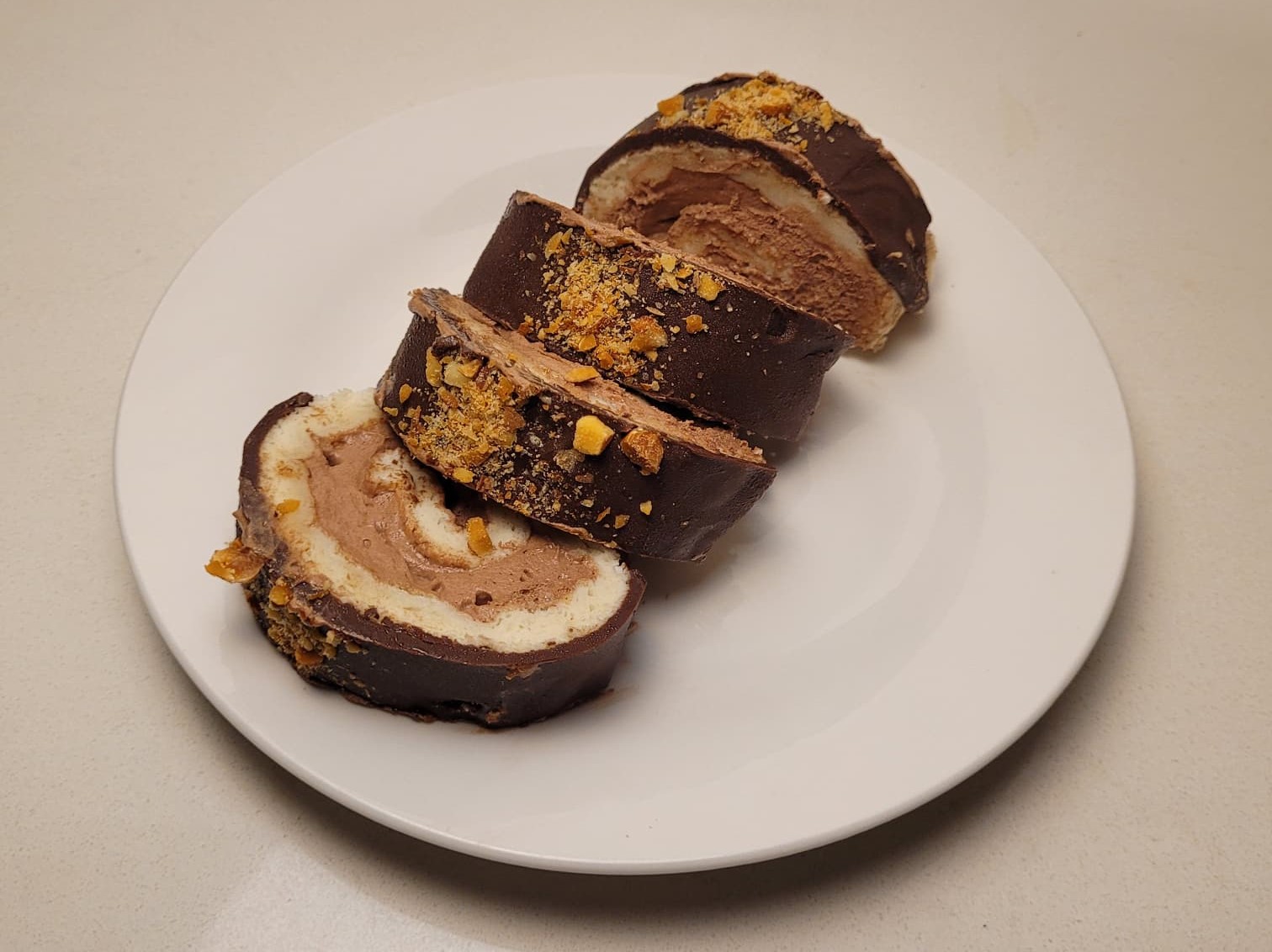 Chocolate Swiss roll slices filled with chocolate cream, coated in chocolate and topped with crushed caramelized nuts